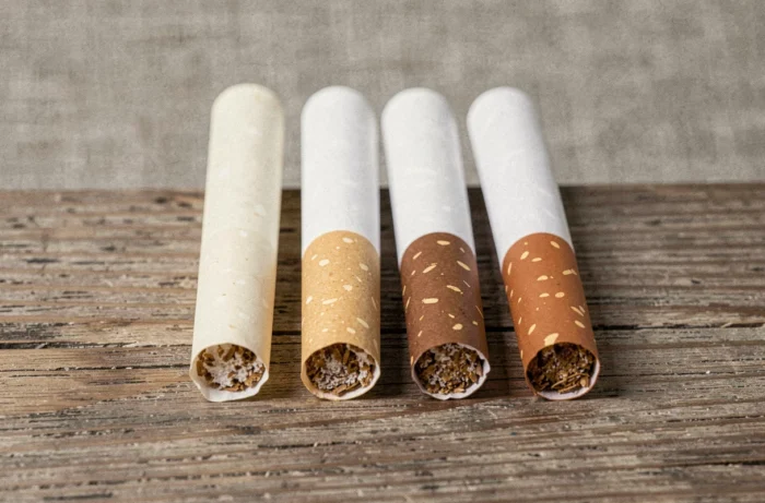 Trois cigarettes Vogue alignées montrant des filtres de couleurs différentes sur une table en bois, illustrant les variations de filtre et de goudron