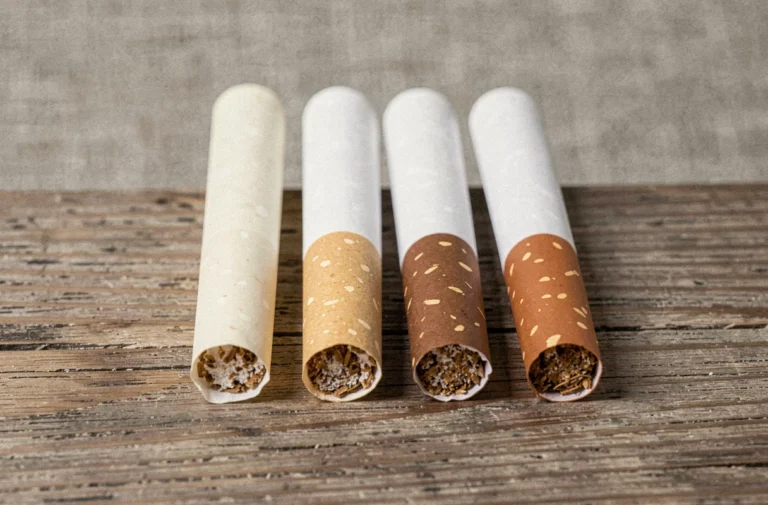 Trois cigarettes Vogue alignées montrant des filtres de couleurs différentes sur une table en bois, illustrant les variations de filtre et de goudron